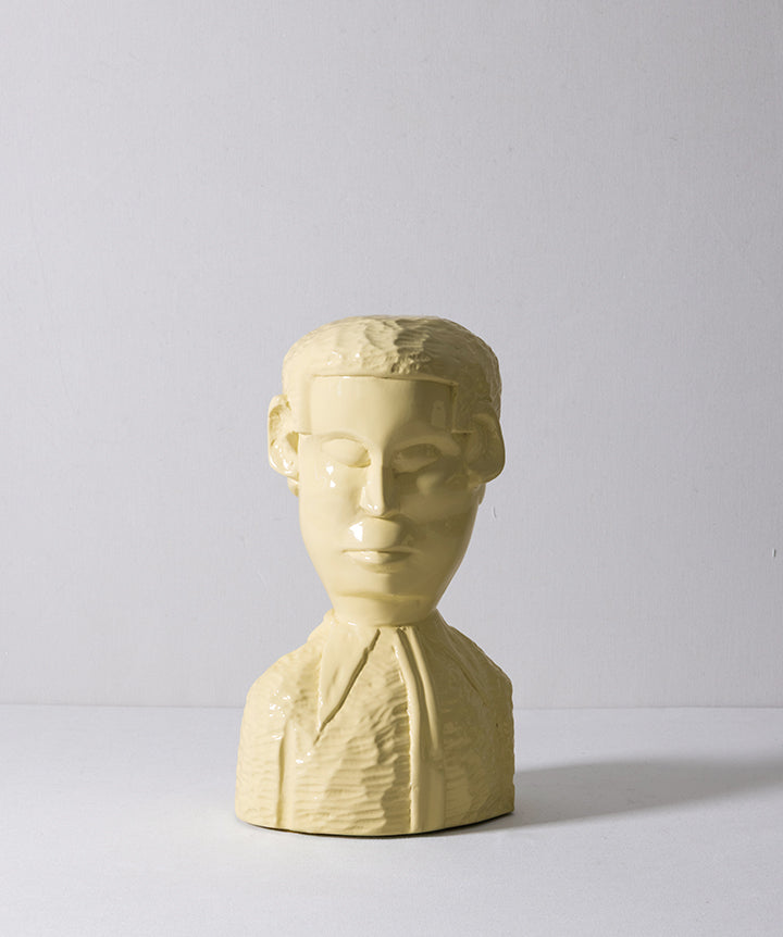 A pale yellow sculptural bust of a man's head and upper torso, photographed against a plain light gray studio background.