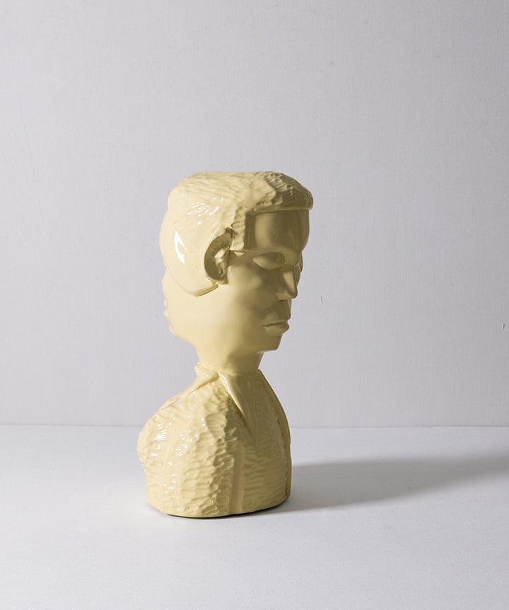 A glossy pale yellow ceramic bust sculpture of a man's head and upper shoulders, shown in profile against a neutral light gray background.