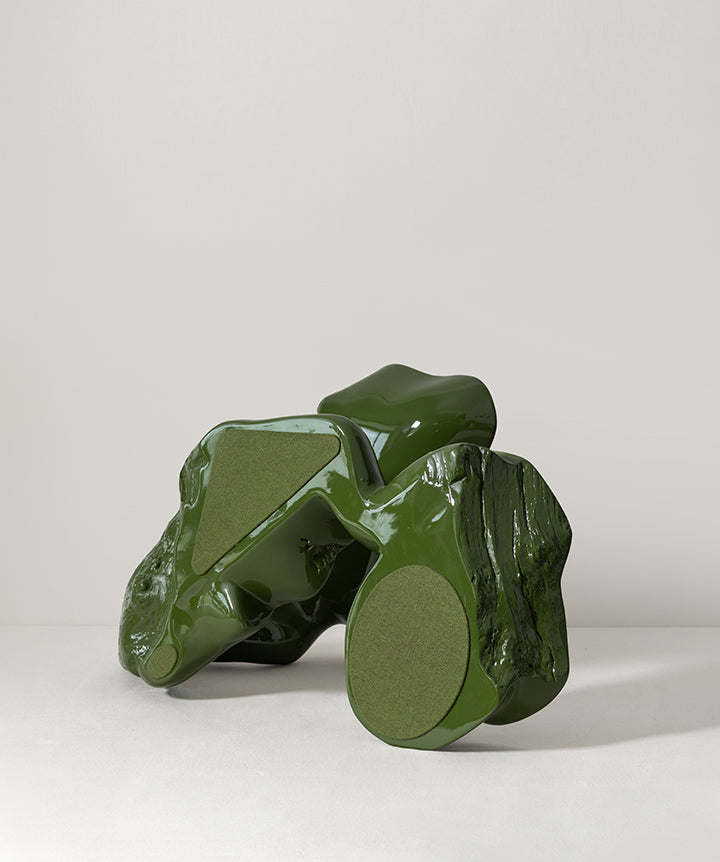 The base of a glossy dark green sculptural ceramic fruit stand shaped like twisted branches or leaves, photographed against a plain light gray studio background.